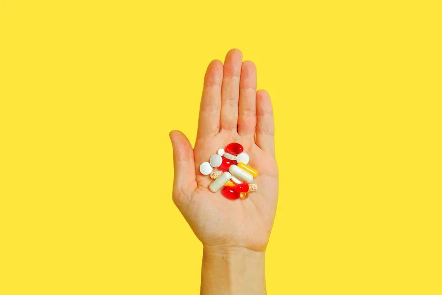 A hand holding assorted supplement pills and capsules